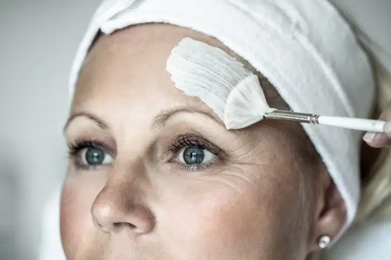 Frau wird eine Gesichtsmaske mit dem Pinsel aufgetragen