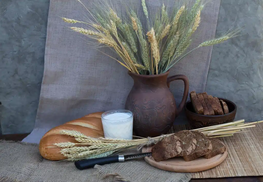 Brot, Weizen und ein Glas Milch auf einem Brett