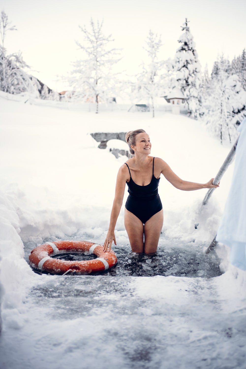 Frau steigt zum Eisbaden in den zugefrorenen Naturbadeteich