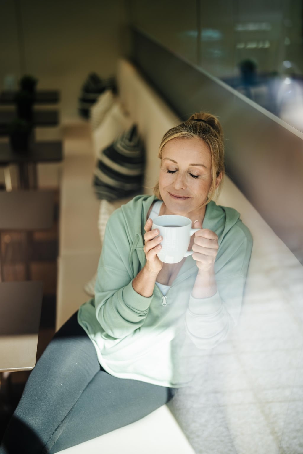 Frau sitzt am Fenster und genießt eine Tasse Tee