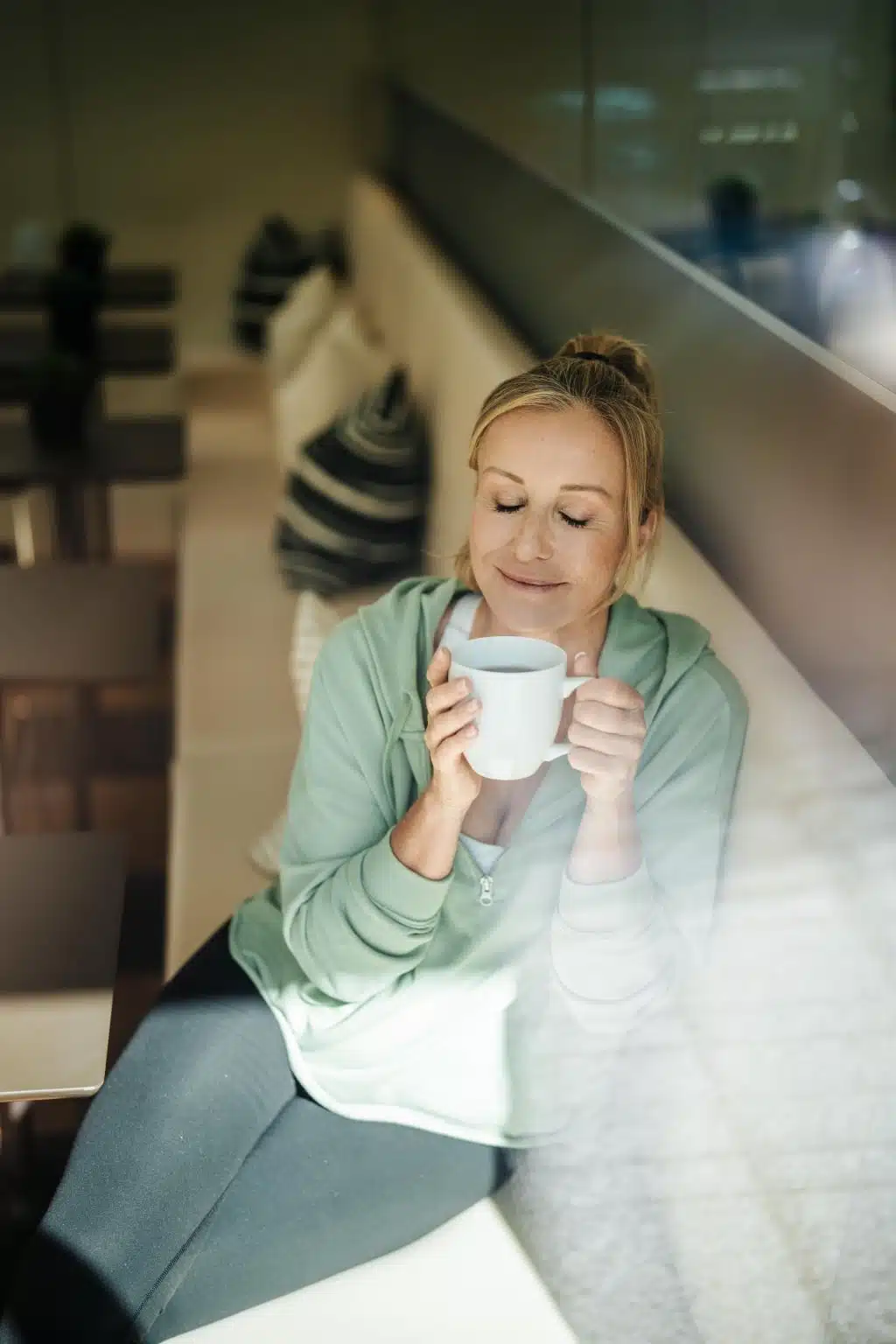Frau sitzt am Fenster und genießt eine Tasse Tee